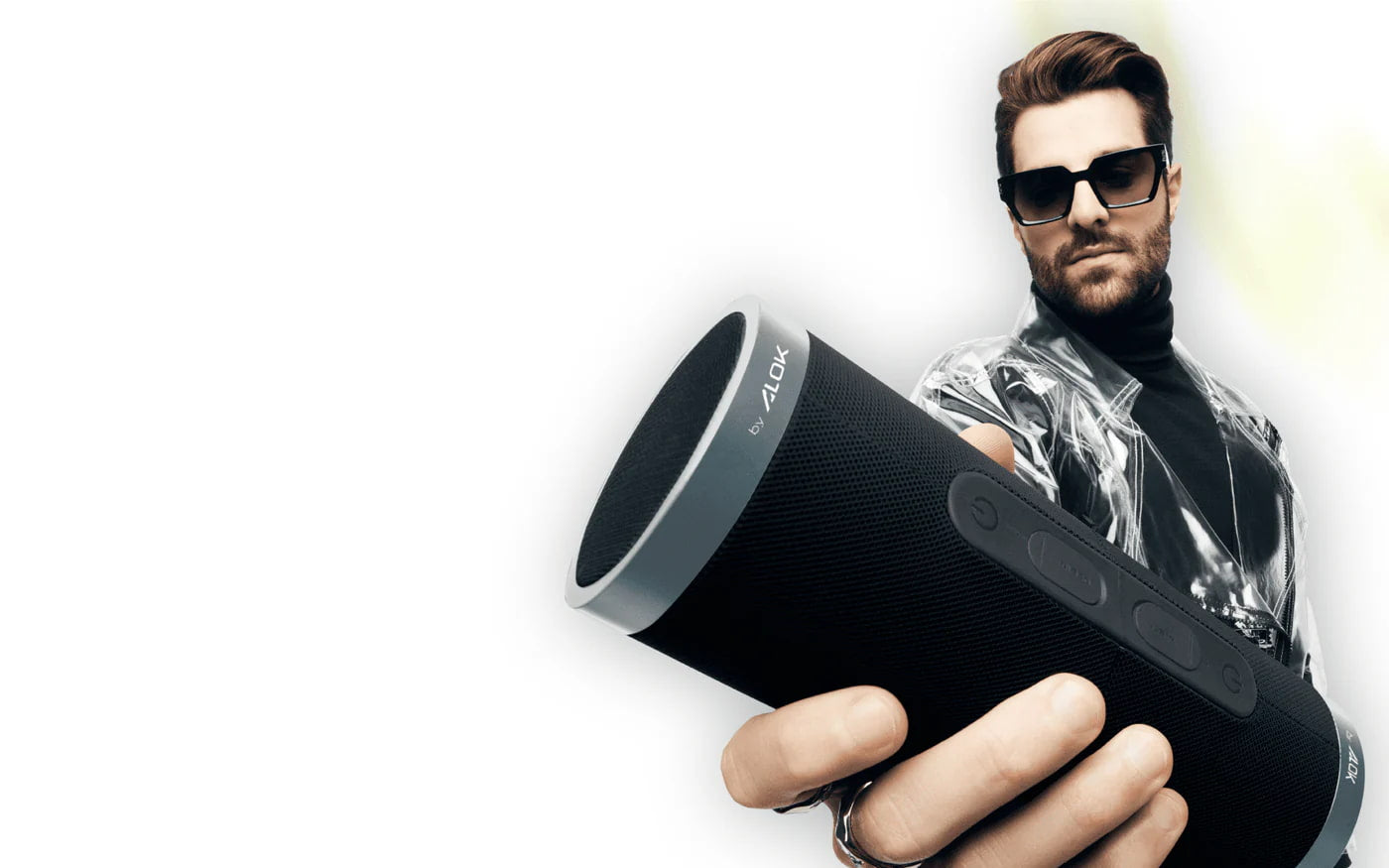 Alok segurando uma caixa de som Bluetooth da marca WAAW, com fundo branco e estilo moderno.