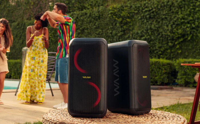 Duas caixas de som torre WAAW com luzes vermelhas, em ambiente externo com pessoas se divertindo.
