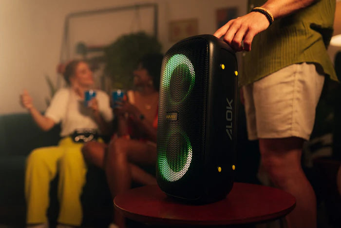 Caixa de som torre WAAW com luzes verdes, enquanto uma pessoa a segura e outras se divertem.